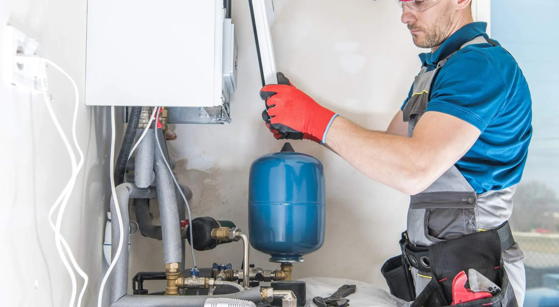 Technician in red gloves servicing a wall-mounted water heater and expansion tank