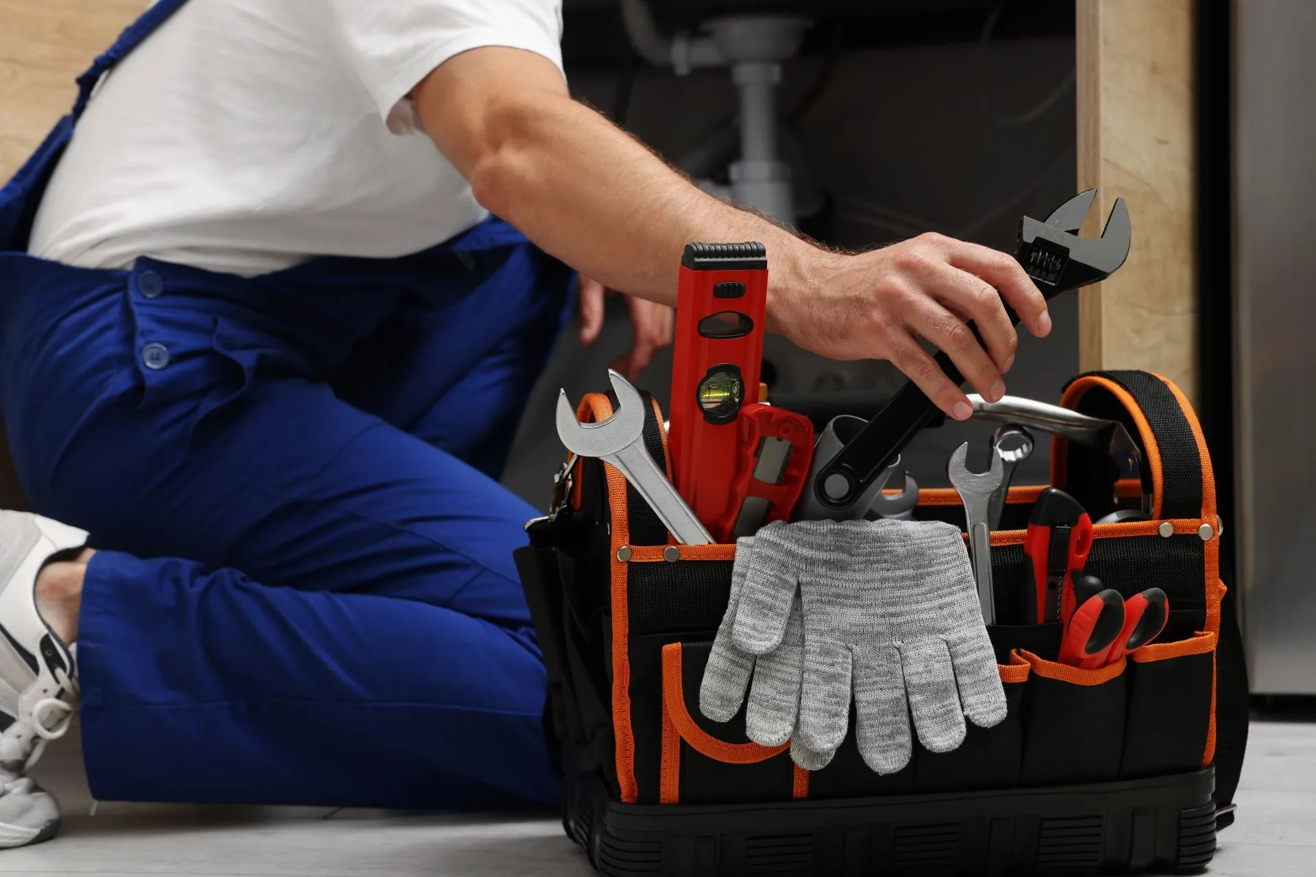 Plumber reaching into a tool bag filled with wrenches, a level and work gloves