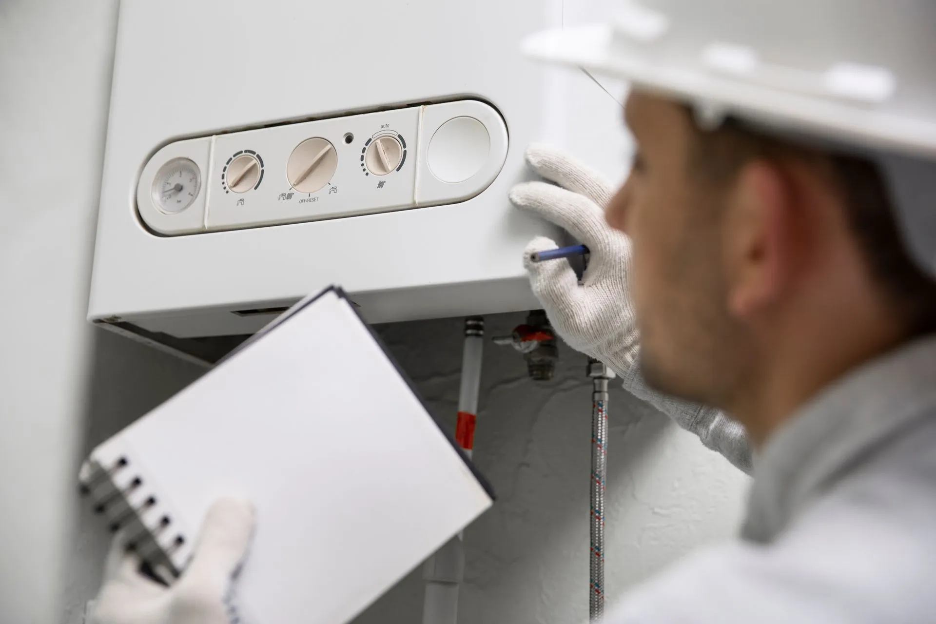 A man is holding a notebook and a pen while working on a boiler.